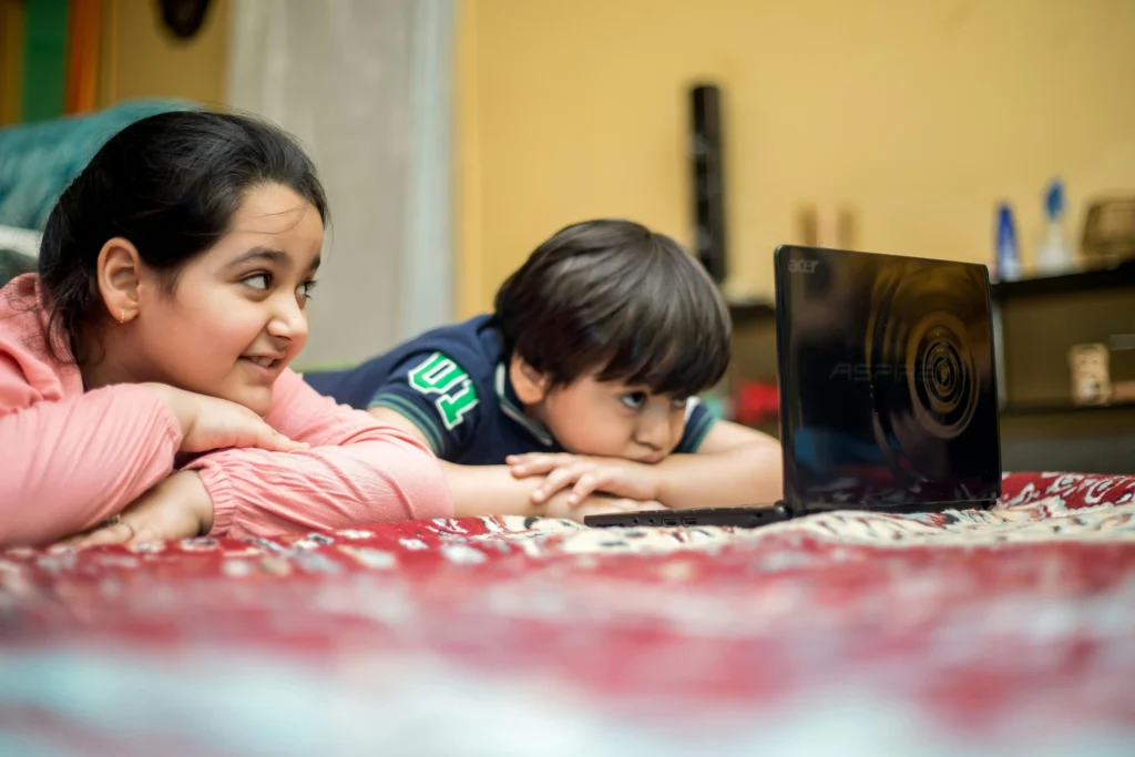 dua anak sedang rebahan dapn menonton video di laptop